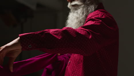 an older man with a white beard adjusts his pink shirt.