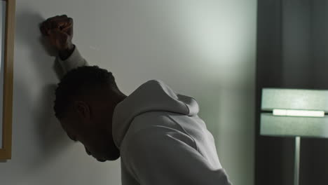 young man with mental health issues standing leaning against wall at home looking depressed and unhappy