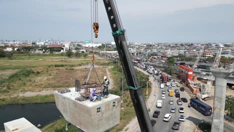 aerial view of bridge construction with crane lifting concrete segment and workers overlooking city traffic