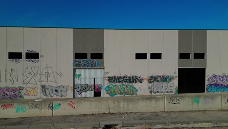 Graffiti-covered-warehouse-wall-under-blue-sky,-Abrera,-Barcelona,-Spain,-urban-art,-aerial-view