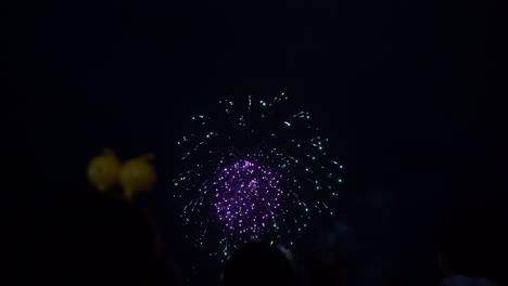 Brillantes-Fuegos-Artificiales-Explotando-Sobre-El-Oscuro-Cielo-Nocturno-Con-Siluetas-De-Personas