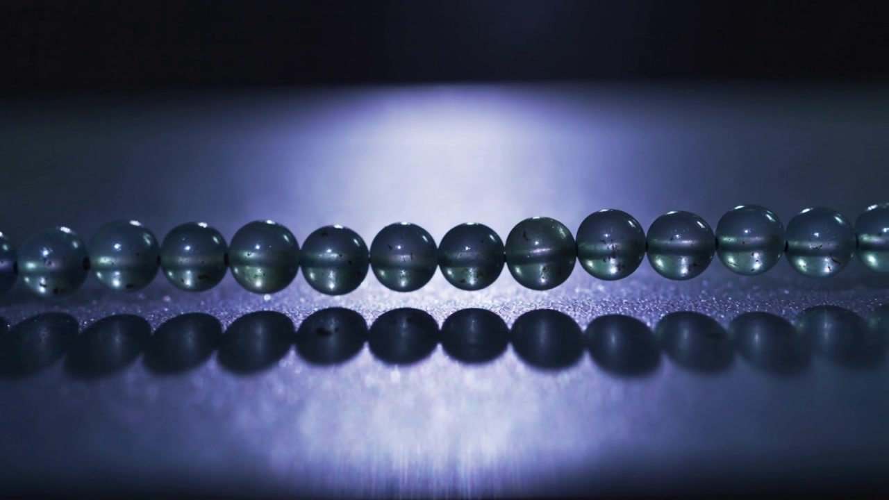 Luce bluastra mutevole che proietta punti luce su perline in studio, enfatizzando superfici e riflessi.