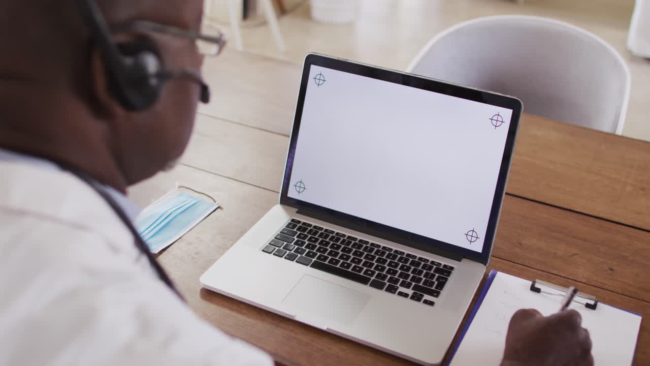 African american male doctor making video consultation wearing headset using laptop with copy space