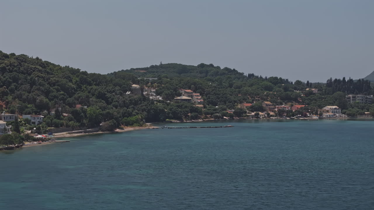 Corfu Island Greece Aerial v5 zoomed flyover calm sea capturing a picturesque coastal village with buildings nestled among lush, green hillsides in summer - Shot with Mavic 3 Pro Cine - July 16th 2024