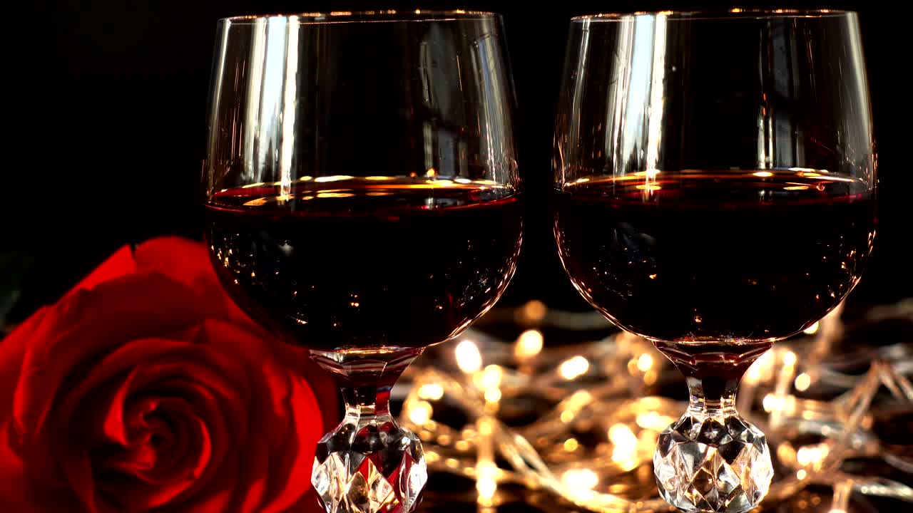 Taça com vinho e uma rosa contra o fundo de guirlandas brilhantes
