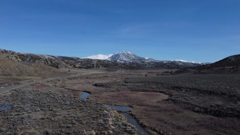 zoom-out drone shot of snow-covered mountain and river-carved valley on a sunny winter day in northern nevada. the dry landscape is covered by brown shrub and contrasted by the white snow and blue sky