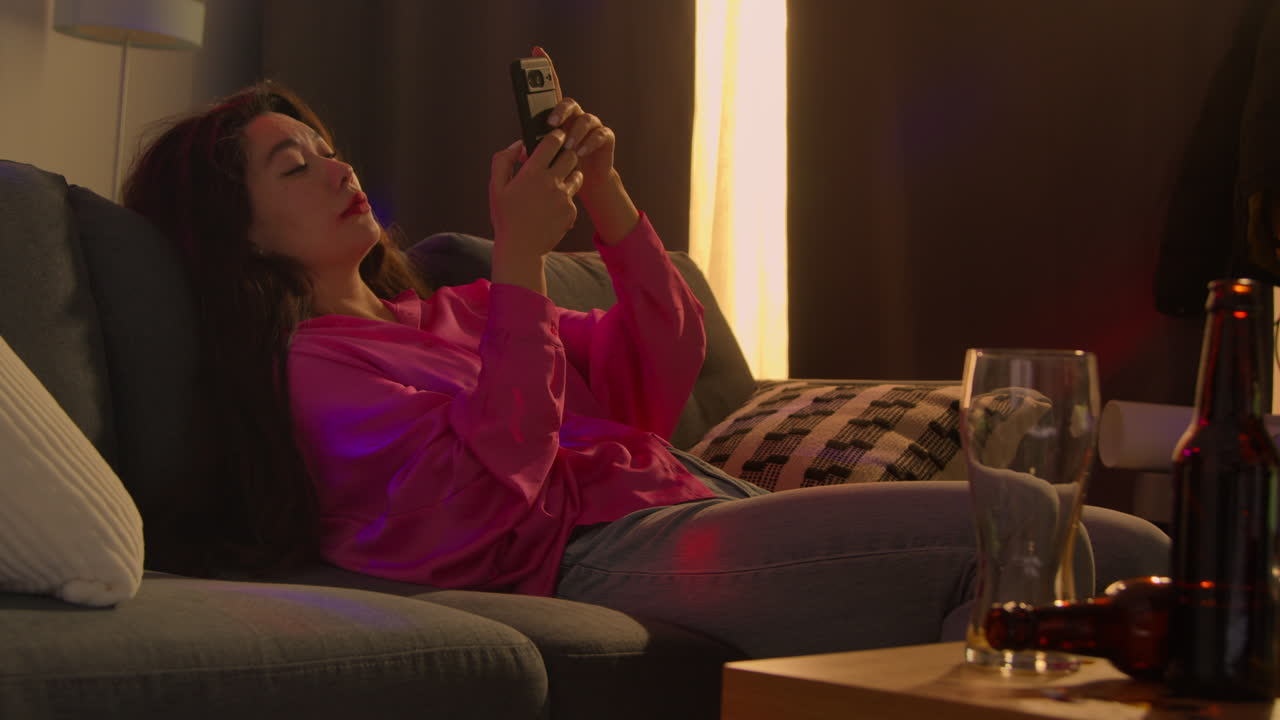 mujer sentada en el sofá después de beber alcohol en una fiesta de casa sufriendo de resaca comprobando mensajes de teléfono móvil
