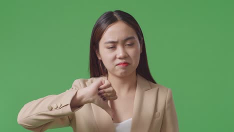 close up of asian business woman showing thumbs down gesture while standing in the green screen studio