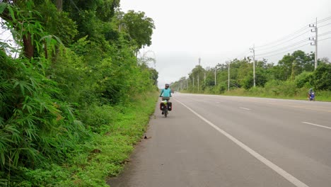 toma trasera de una deportista montando una bicicleta en el arcén de una carretera del sudeste asiático