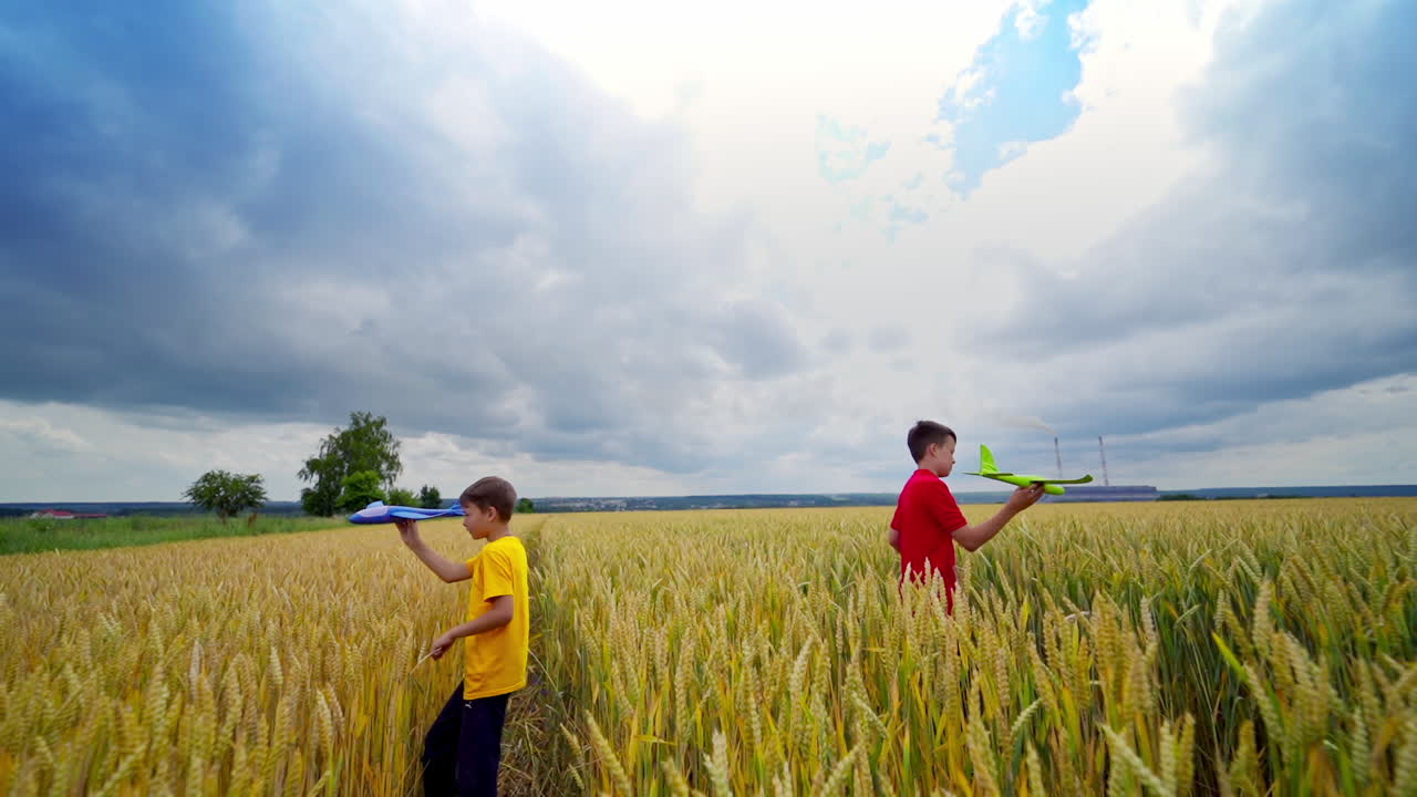 Two happy boys playing with toy plane in wheat field. Cloudy sky. Video of playing process. Summer and vacation concept.