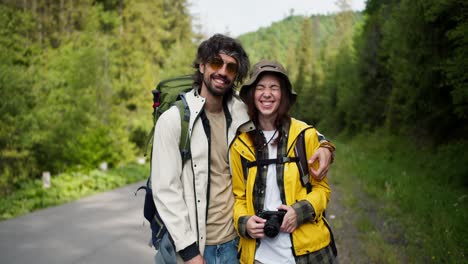 A-guy-and-a-girl-tourists-in-special-clothes-for-hiking-pose-with-a-camera-against-the-backdrop-of-a-mountain-forest