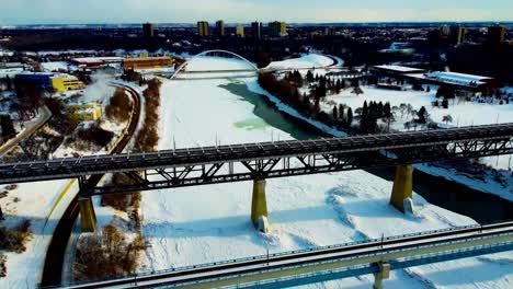 Winter-afternoon-aerial-flyover-drop-dolly-roll-birds-eye-view-over-bridges-of-public-transit-high-level-and-white-modern-walter-dale-North-Saskatchewan-River-inbetween-Victoria-Kinsmen-Park-blu3-4