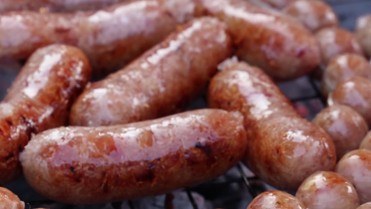 Close-up of sausages and meatballs grilling, tongs turning food, smoky, natural light, shallow focus