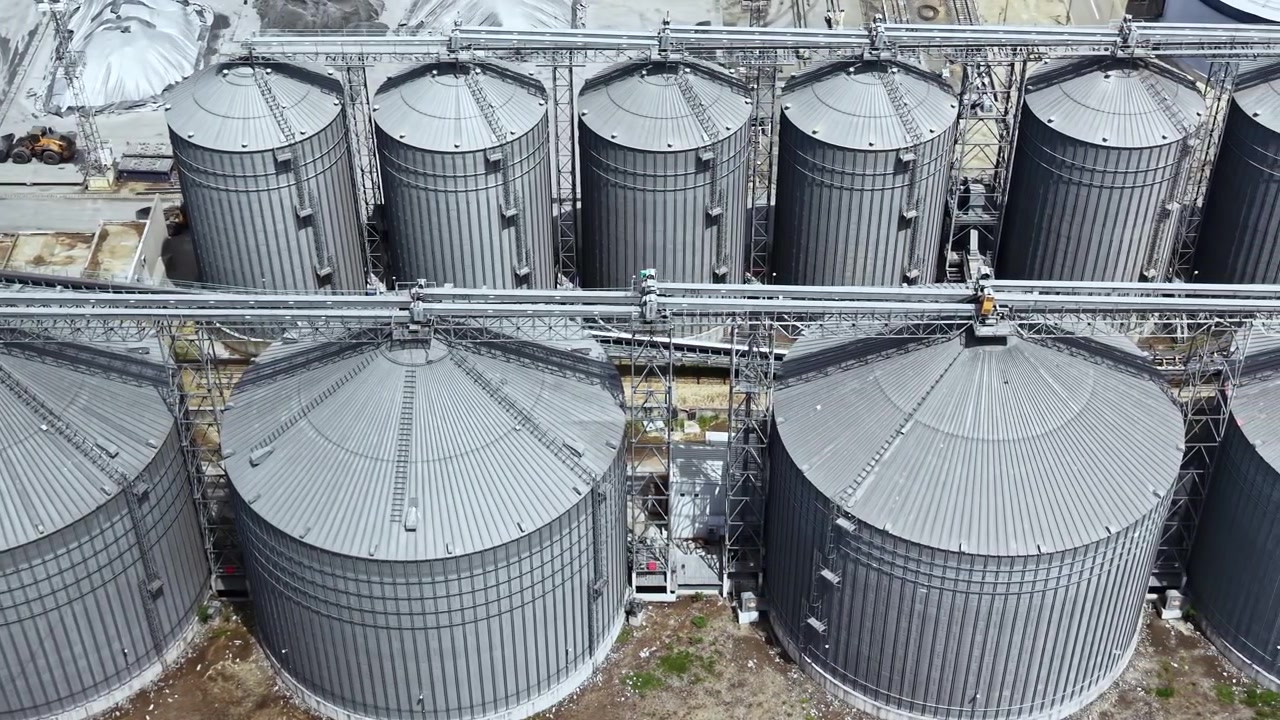 Ansicht von Lagersilos in einer Getreideanlage, die mehrere große Metallstrukturen und Maschinen bei Tageslicht zeigt.