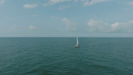 Aerial-establishing-view-of-a-white-sailboat-in-the-calm-Batltic-sea,-white-sailing-yacht-in-the-middle-of-the-boundless-sea,-sunny-summer-day,-wide-done-orbit-shot