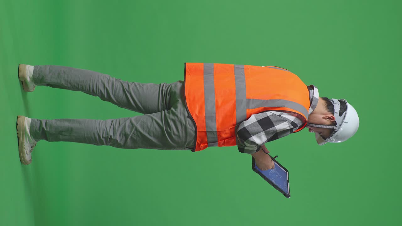 Full Body Back View Of Asian Male Engineer With Safety Helmet Using A Tablet Drawing The Wind Turbine Blueprint While Standing In The Green Screen Background Studio
