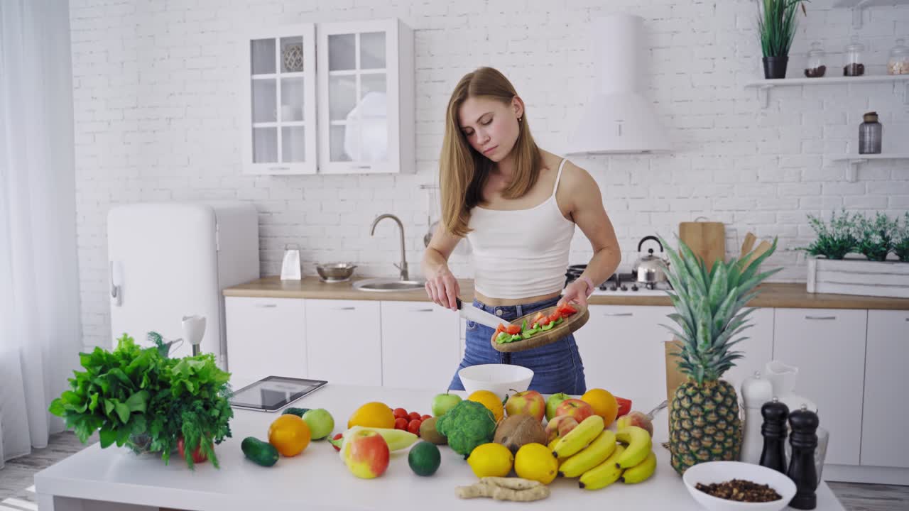 Young pretty woman preparing tasty salad on the modern kitchen. Lots of fresh organic ingredients on the table indoors. Healthy food. Dieting concept.