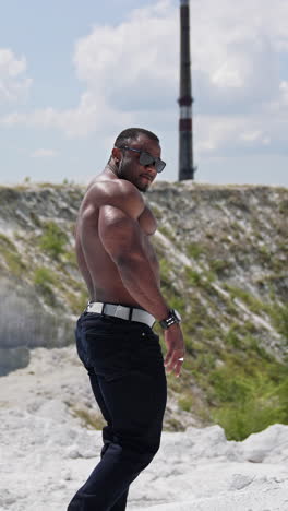 athletic african man without shirt walks on hill. muscular dark skinned sportsman among nature in summer. slow motion. vertical video