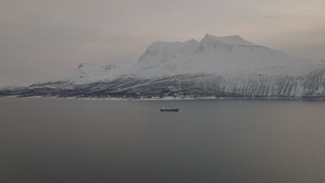 挪威特羅姆索 (tromso) 的克瓦洛亞 (kvaløya) 沿著雪山的海峡航行的一艘貨船