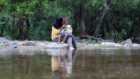 isolated women spending quality time with son sitting on stone at calm lake shore in the morning