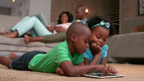 siblings using tablet pc on the floor