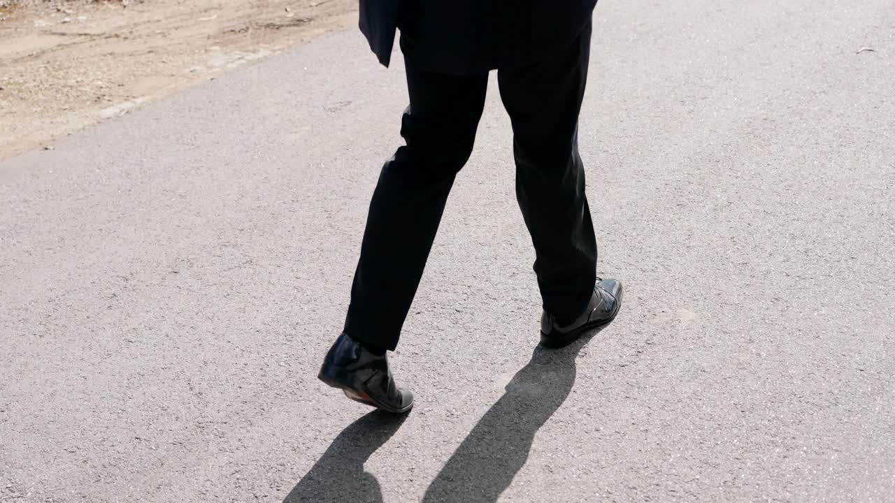 Low angle of man in suit walking on sunlit asphalt road