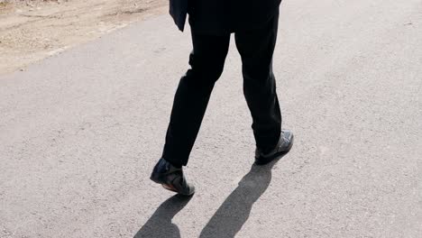 low angle of man in suit walking on sunlit asphalt road
