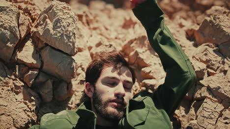 Dramatic-top-down-tight-shot-of-Israeli-man-with-eyes-closed-falling-backwards-onto-jagged-rocks-in-Judean-desert-in-daylight