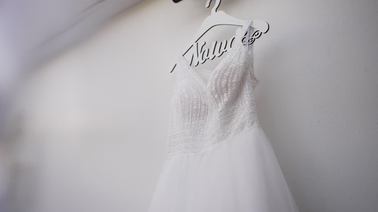 elegant white wedding dress with intricate beading on a hanger, casting soft shadows on a light wall