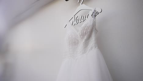 elegant white wedding dress with intricate beading on a hanger, casting soft shadows on a light wall