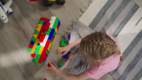 Girl-with-braid-sits-on-rug-building-wall-from-constructor