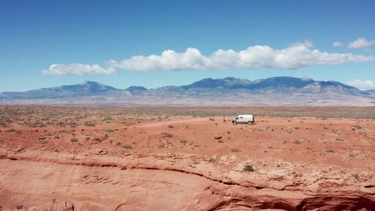 Arizona, Marble Kanyonu'nda kırmızı kanyon falez kenarına park etmiş karavan minibüsün sinematik havadan çekimi.