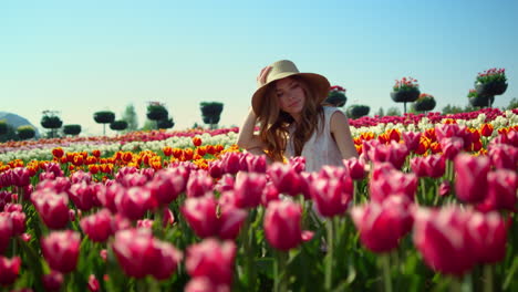 Camera-tracking-aroung-pretty-girl-in-sunhat-sitting-in-pose-in-red-tulip-field.