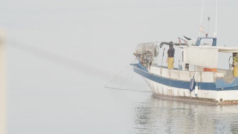 Small-fisherman-boat-collecting-fishing-net-with-two-workers-in-calm-sea-at-sunrise-in-slow-motion-60fps