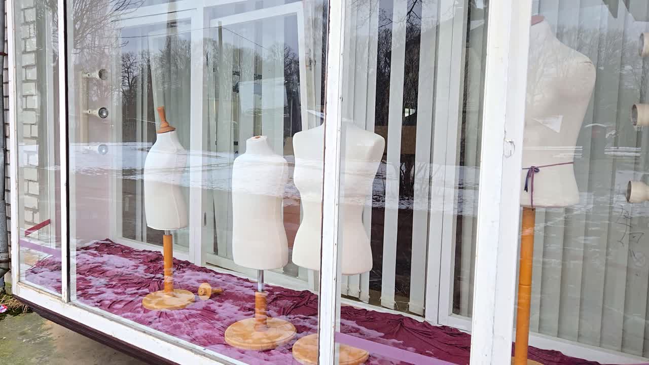 Tomme mannequiner står i butiksvindue og afspejler en stille gade udenfor.