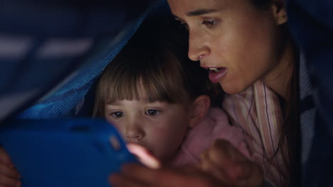 Glückliche-Mutter-Und-Kind,-Die-Einen-Tablet-Computer-Unter-Einer-Decke-Benutzen.-Kleines-Mädchen-Spielt-Spiele-Auf-Touchscreen-Technologie-Und-Hat-Vor-Dem-Schlafengehen-Spaß