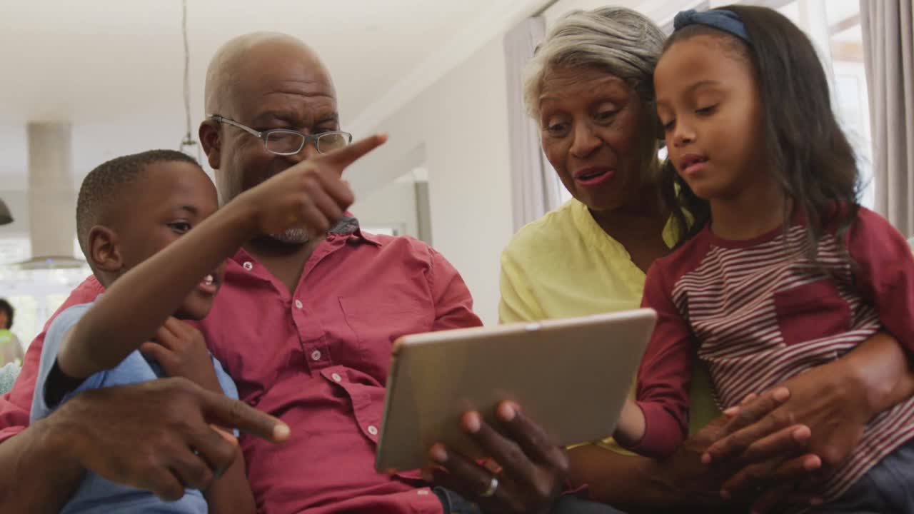 Video of happy african american grandparents and grandchildren using tablet together