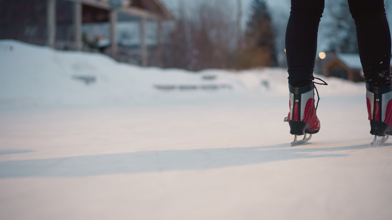 Closeup of person skating on outdoor rink during winter, red skates moving swiftly over ice surface, snow and blurred background lights adding seasonal atmosphere, showcasing energy, speed, and motion