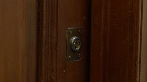 Close-up-on-hand-turning-key-locking-old-wooden-brass-door-keyhole-lock