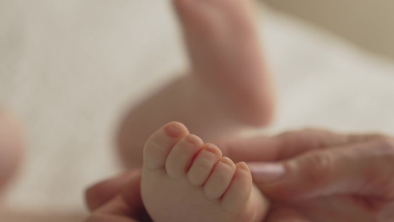 Nærbillede af nyfødt babys fødder og fingre, mor masserer cirkler med hænderne
