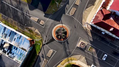 overhead drone footage captures vehicles navigating a small city roundabout surrounded by commercial buildings in bright daylight, highlighting urban infrastructure and traffic flow