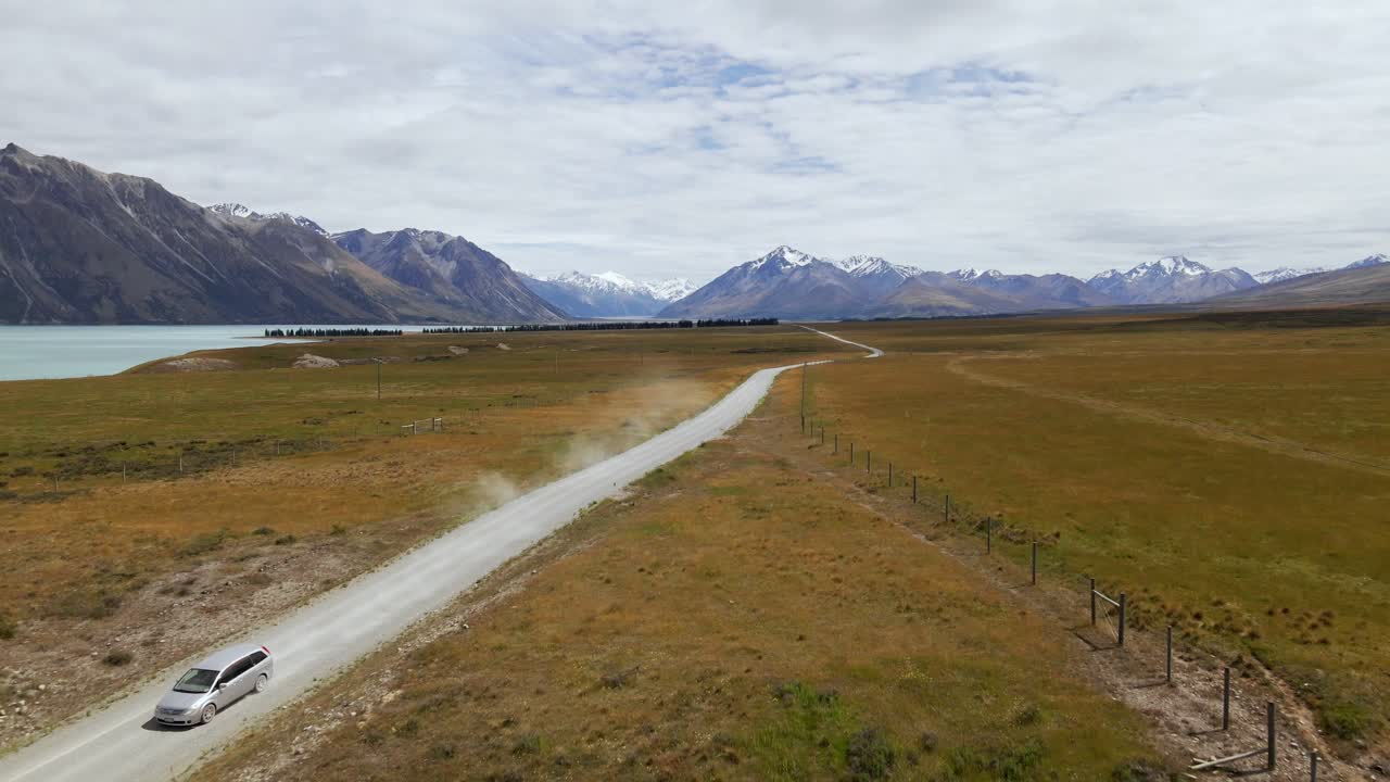 눈 덮인 산들을 배경으로 먼지투성이의 그림 같은 흙길에 있는 은색 밴