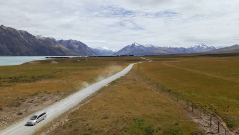 silver van on dusty, picturesque dirt road with snow-capped mountains in background