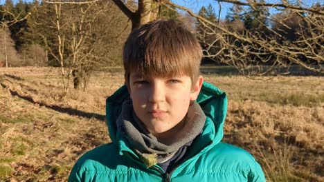 good looking boy is standing outdoors in forest, modeling for the camera