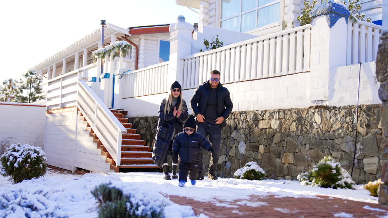 Happy parents standing at the stairs to their cottage. Couple is clapping to their baby boy running towards camera.