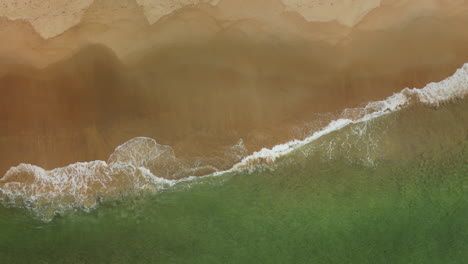 Slow-rising-aerial-shot-overhead-waves-rolling-onto-a-beach-in-Norway