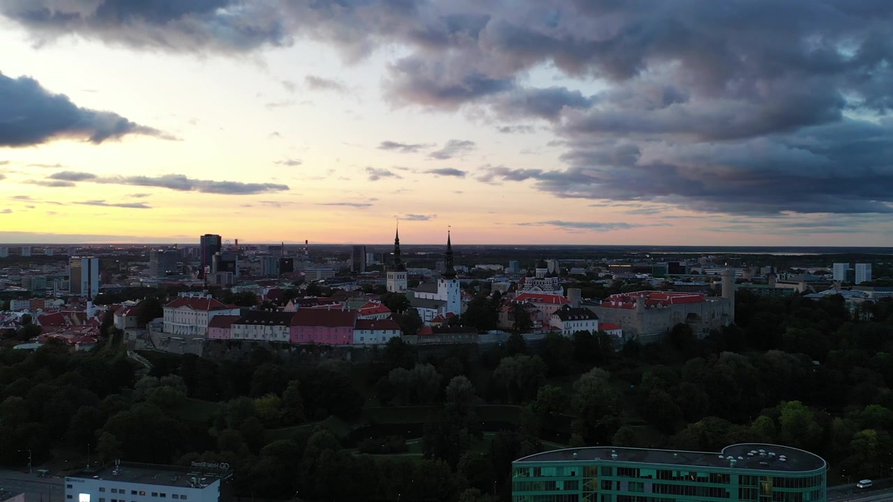 Filmato mozzafiato con drone del Centro Storico medievale di Tallinn al tramonto. L'inquadratura mostra la Collina di Toompea, la Cattedrale di Santa Maria e gli edifici dai tetti rossi sotto un cielo drammatico di nuvole rosa e arancioni.