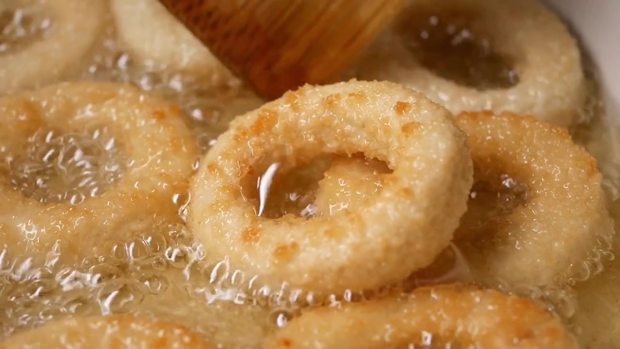 Anelli di cipolla che friggono in olio caldo in padella.