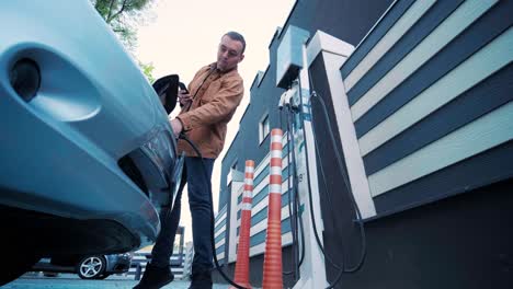 proceso de reabastecimiento de combustible de un automóvil eléctrico. un disparo debajo de la escotilla donde se carga el automóvil ecológico eléctrico. la escotella de carga del automóvil eléctrico se abre automáticamente. una mano masculina inserta un automóvil erecto