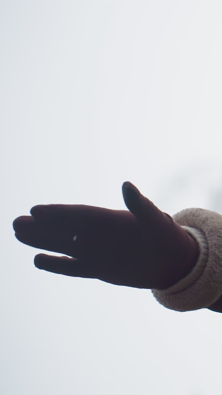 Close-up shot of lady in black cap and brown shearling jacket, arms outstretched, walking joyfully in cool autumn weather. Her body is partially visible, enjoying nature outdoors